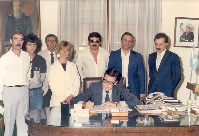 En 1986, durante la firma de la escritura correspondiente al terreno de la Sociedad de Fomento de Barrio Parque «Julio de Vedia». De izq. a der., Carlos De Sogos, Roberto Lafulla, escribano Jorge Cardinal, Zulma García, Jorge Giulietti, Héctor Pueblas y Omar Malondra; sentado, el Intendente Municipal Abel De la Plaza .